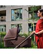 1518099110_F8_2026_maxicosi_stroller_oxfordcarrycot_oaktruffle_lifestyle_momcheckingcarrycotside